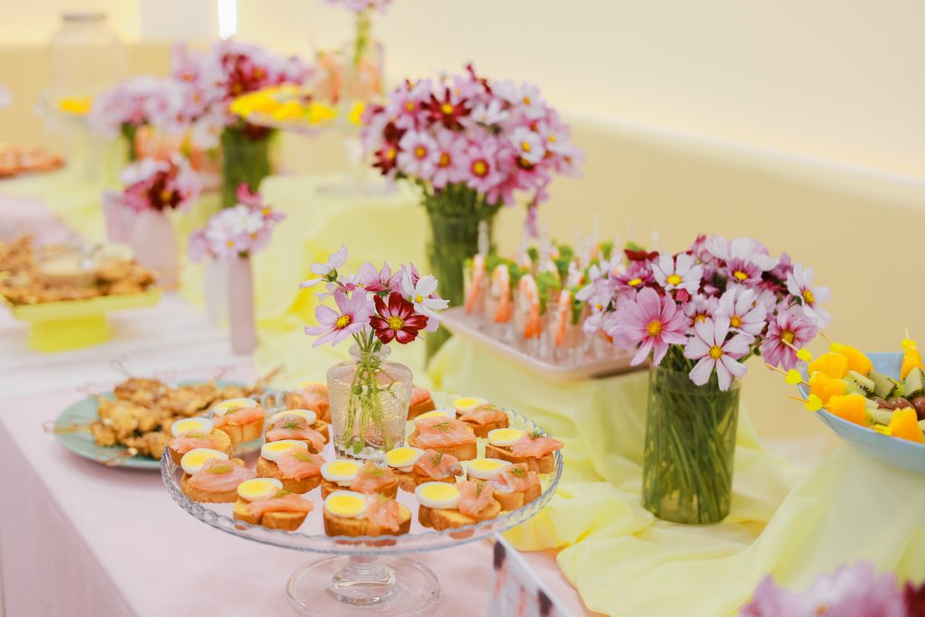 Bàn tiệc sinh nhật trang trí với hoa bướm trong lọ thủy tinh nhỏ, kết hợp cùng finger food và khăn trải màu pastel tạo cảm giác tinh tế như được chuẩn bị bởi chuyên gia