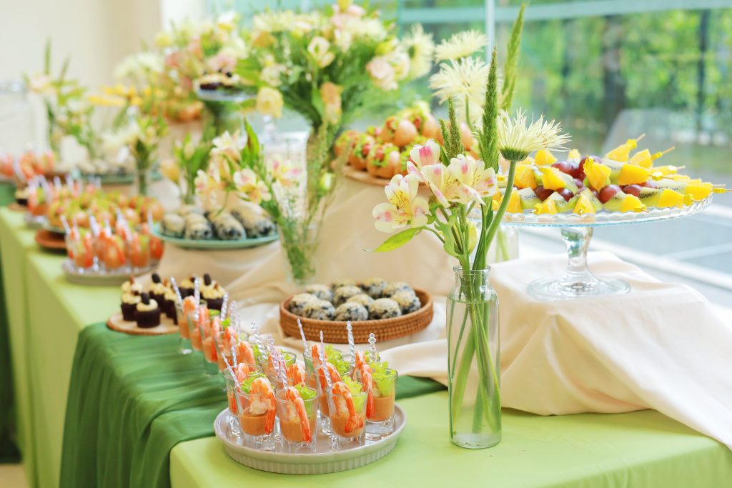 Bàn tiệc finger food được trang trí với nhiều lọ hoa nhỏ bằng chai thủy tinh, tạo điểm nhấn nhẹ nhàng và không khí gần gũi cho tiệc sinh nhật