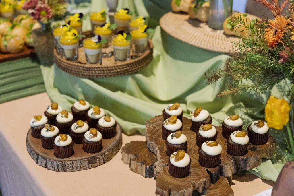 Bàn tiệc finger food với khay cupcake và cheesecake xoài được bày trên khay gỗ và mây, thể hiện sự đồng bộ trong chủ đề trang trí tiệc tại nhà cho bé